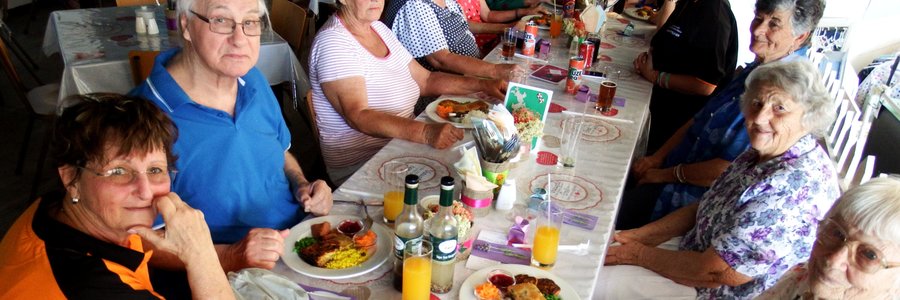 Enkele Gansbaaiers sit gesellig om ‘n tafel en eet tydens die Kersmark, met Maretha Geldenhuys voor links